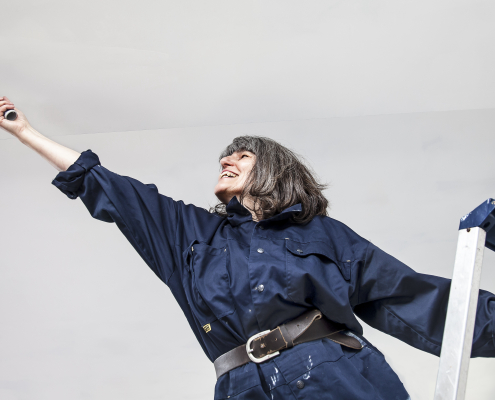 Woman on a ladder, reaching out to paint a ceiling