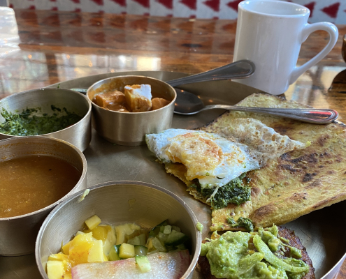 Breakfast thali - brass tray with a variety of Indian foods, and a coffee cup in the background