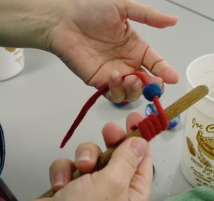 Gika's hands making felt cording, wrapped around a dowel