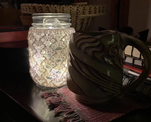 Knitted lace around a glass jar filled with twinkle lights, along with a coffee mug and books in the background.