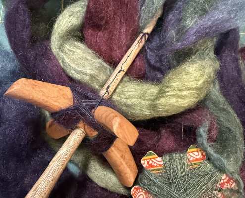 Turkish handspindle lying on loose, purple and green wool and silk fiber, and a bit of handspun yarn