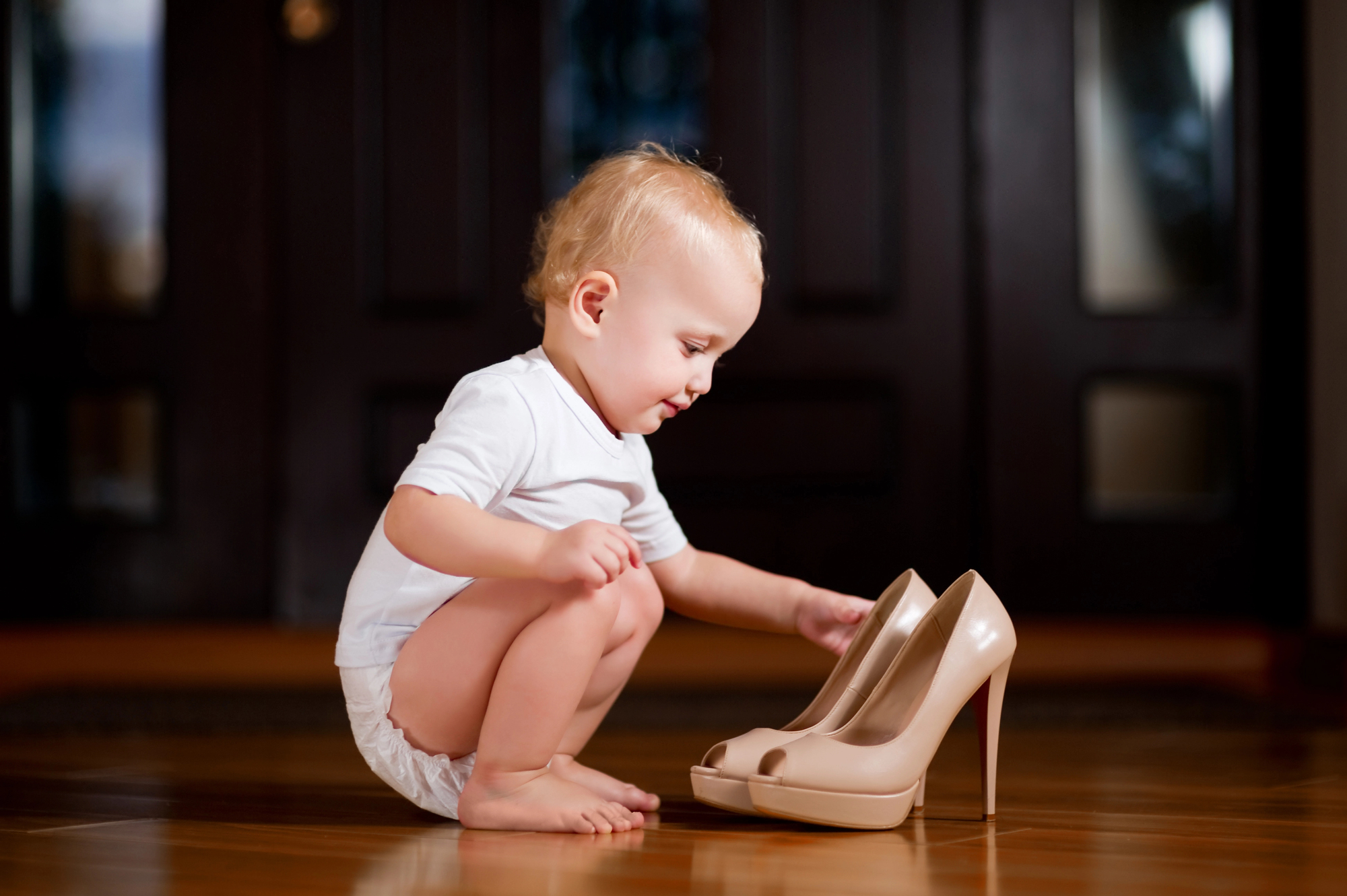 Baby sitting with heels on the ground looking at a pair of high heels