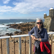 Woman standing in front of a railing with a beach and old stone building in the background