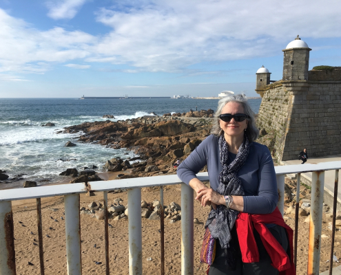 Woman standing in front of a railing with a beach and old stone building in the background