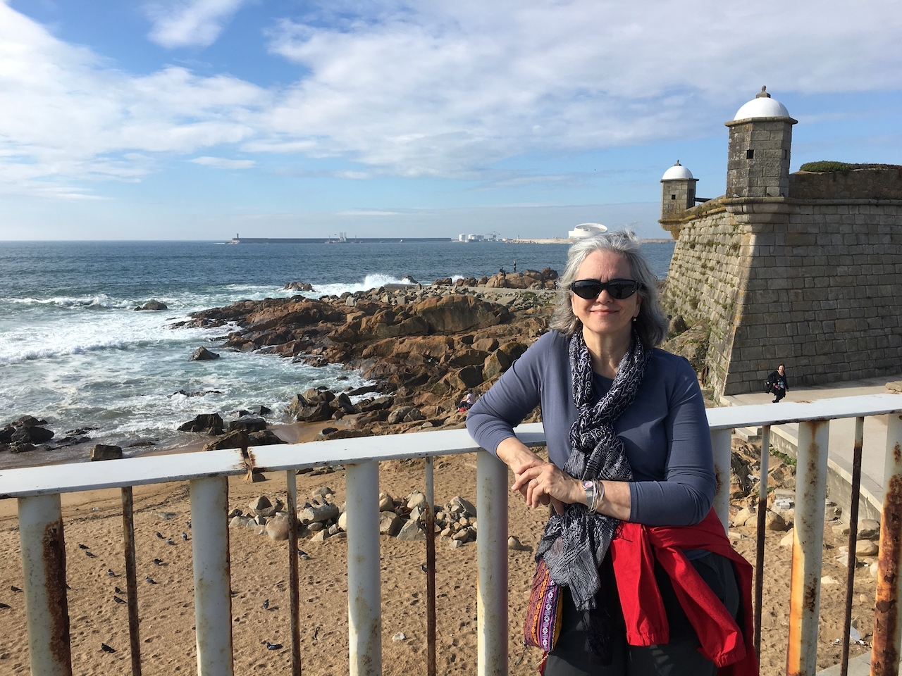 Porto beach view Woman standing in front of a railing with a beach and old stone building in the background