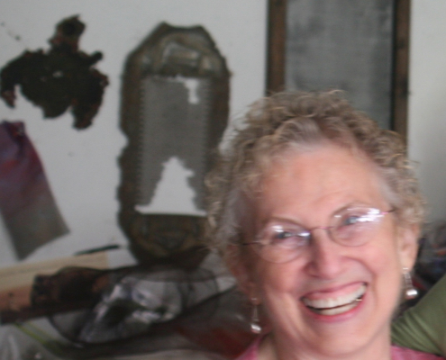 Beth Beede, smiling woman with objects on the wall behind her.